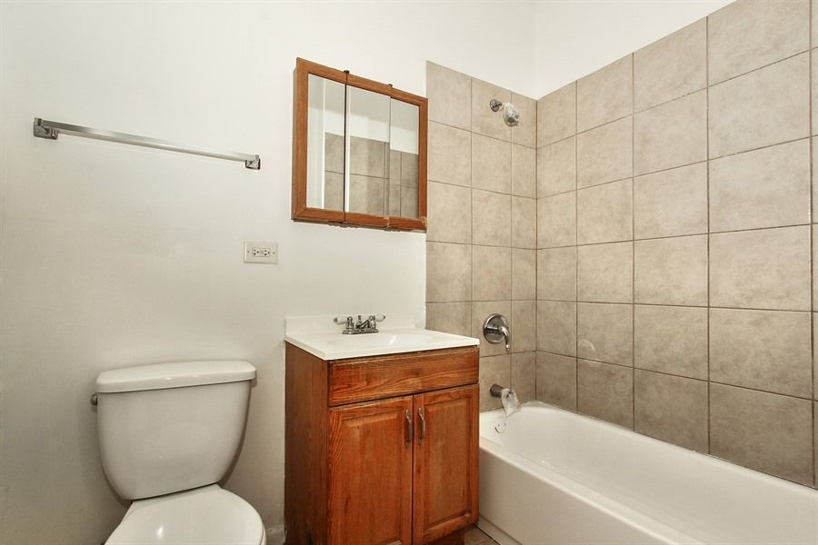 Bathroom with a white toilet, brown vanity, and beige tiled shower.