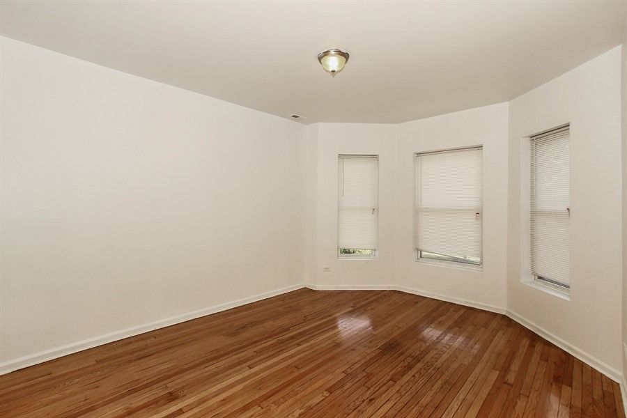 Empty room with hardwood floors, white walls, and three windows.