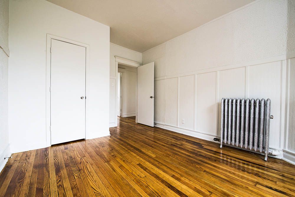 Empty room with wood floor, white walls, and a radiator.