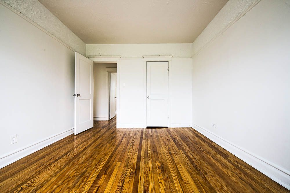 Empty room with hardwood floors, white walls, and a few closed doors.