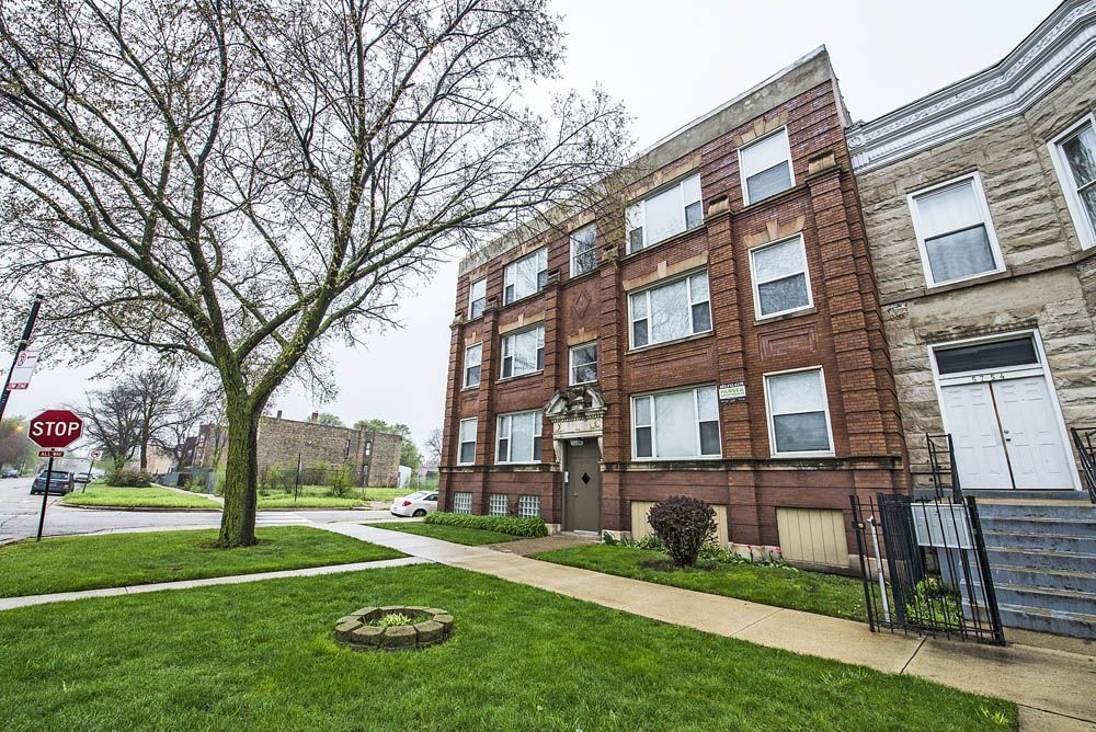 Brick apartment building on a grassy lot, tree in the foreground, stop sign visible.