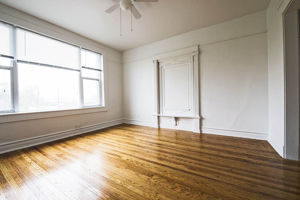 Empty room with hardwood floors, large window with blinds, and decorative wall panel.