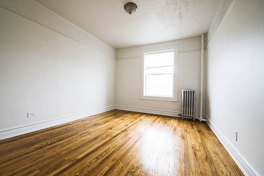 Empty room with wood floors, white walls, window, and radiator.