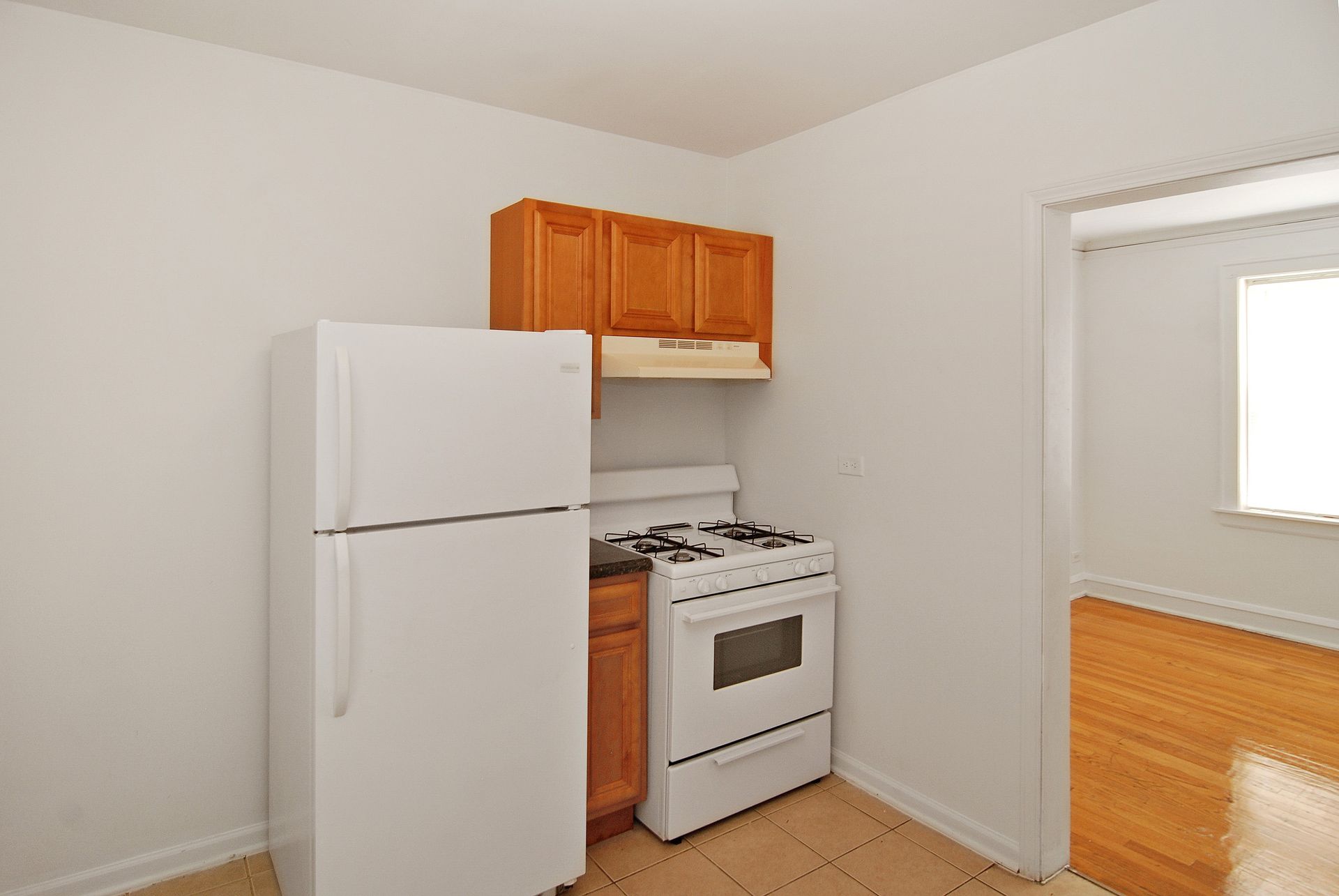 Small kitchen with white appliances, wooden cabinets, and a doorway.