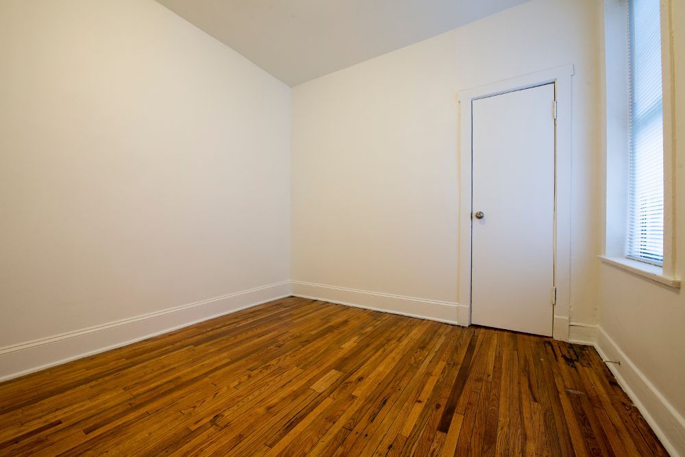 Empty room with wood floors, white walls, and a door and window.