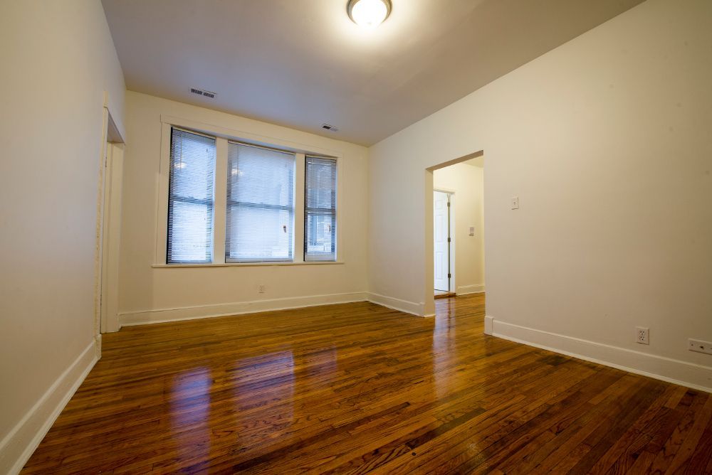 Empty room with hardwood floors, white walls, and a window with blinds.