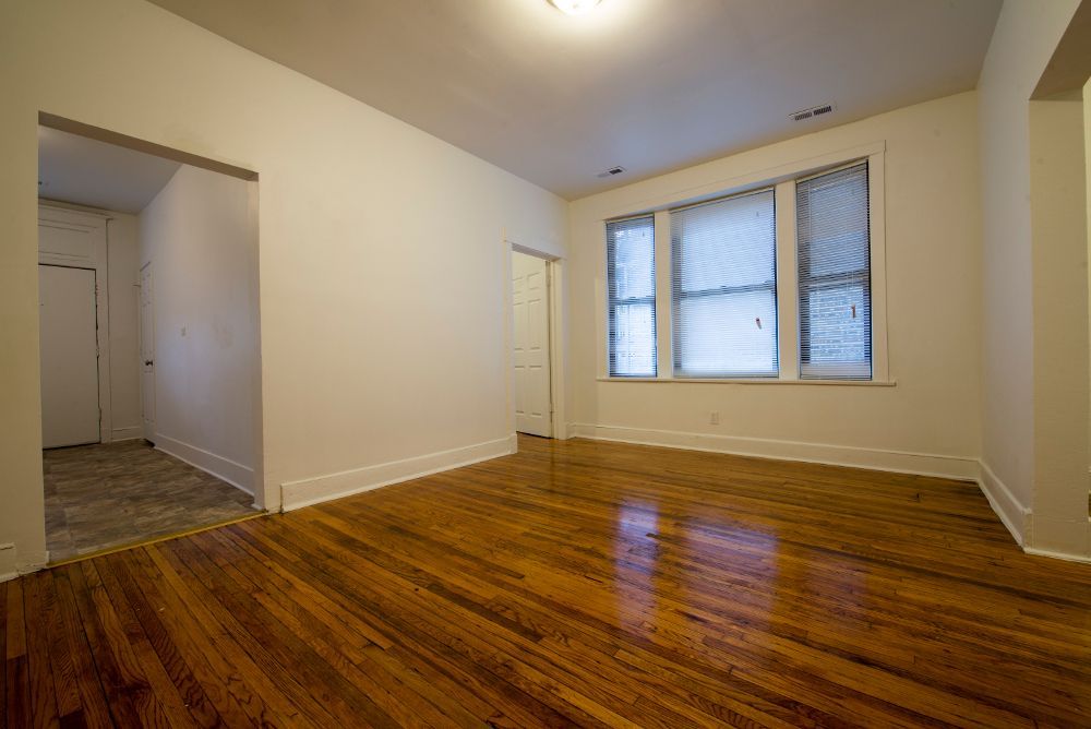 Empty room with hardwood floors, white walls, and a window.