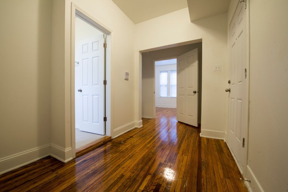 Hallway with hardwood floor, white walls, and three doorways.