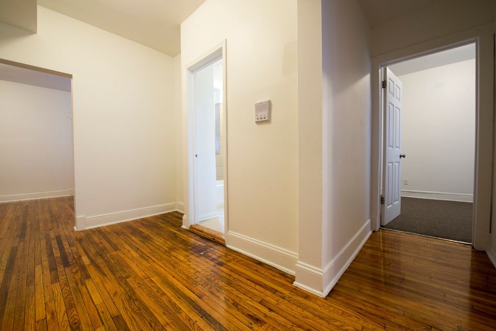 Hallway with hardwood floor, three doorways, white walls.