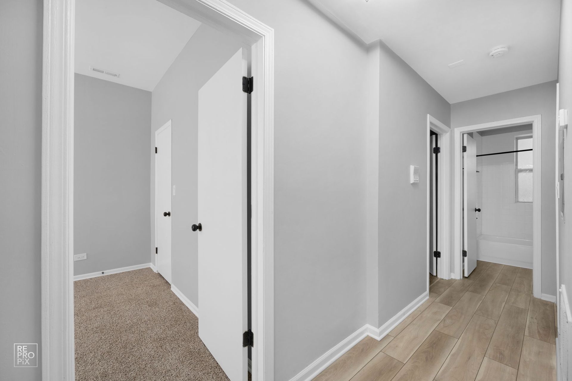 Hallway with gray walls, white trim, and doors. One doorway shows a carpeted room; the other shows a bathroom.
