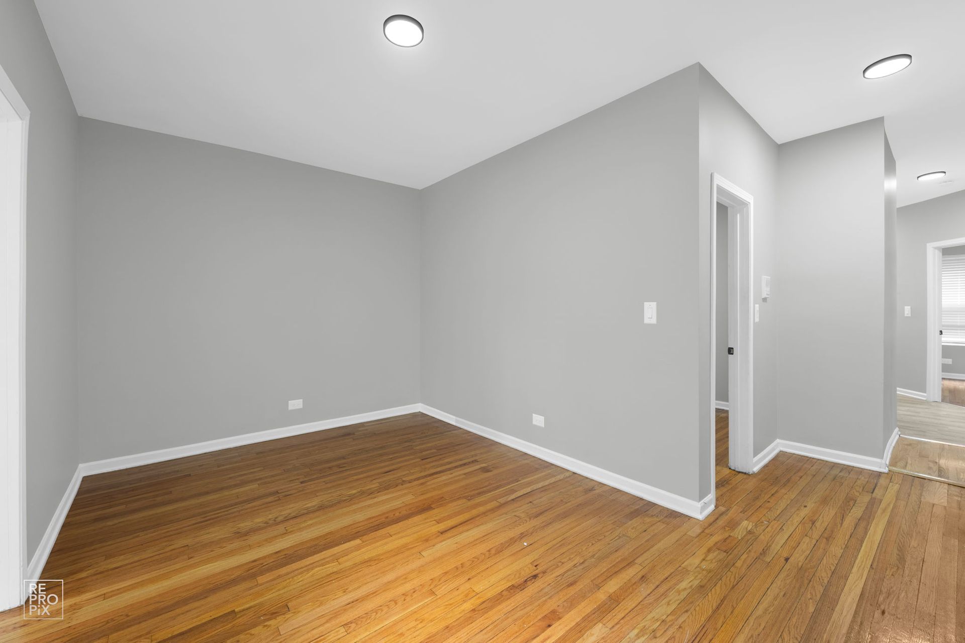 Empty room with gray walls, hardwood floor, and white trim. Doorways lead to other rooms.