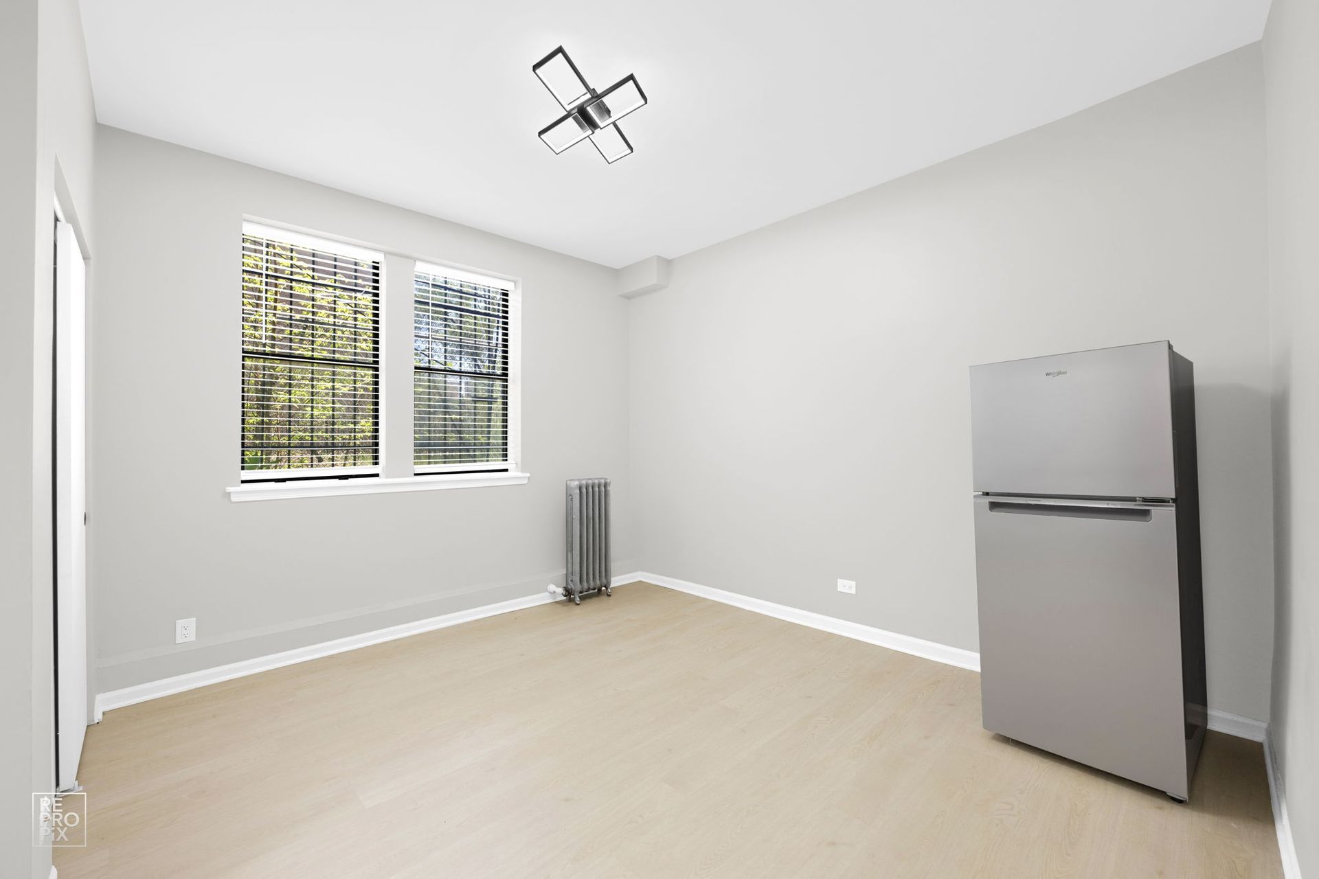 Empty room with light-colored walls, floor, window, and refrigerator.