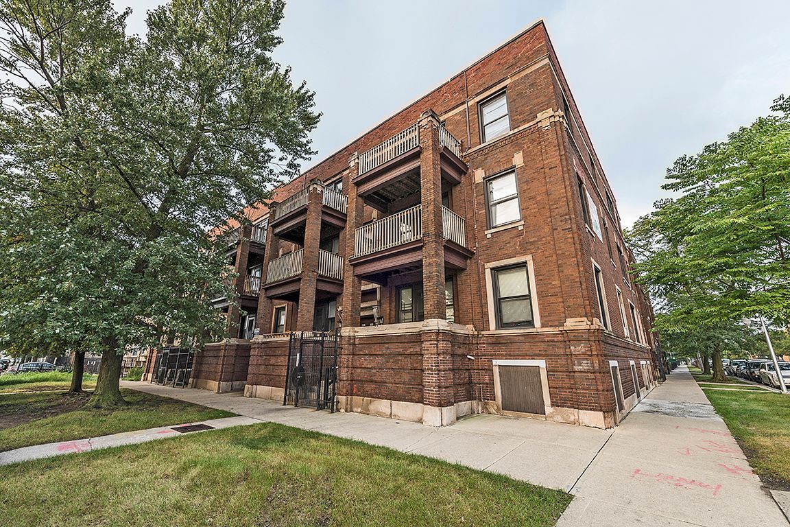 Brick apartment building with balconies, sidewalk, trees.