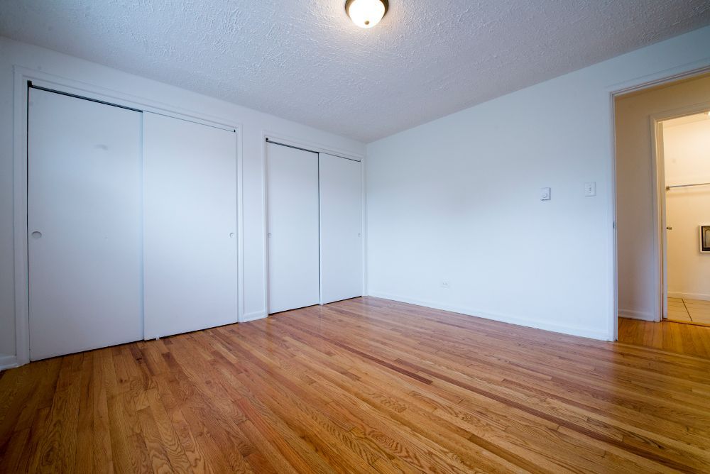 Empty room with hardwood floor, white walls, two closets, and a doorway.