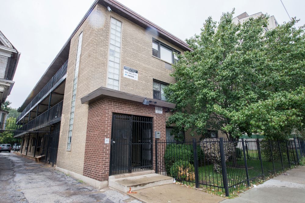 Two-story brick apartment building with black security gates and metal balconies. A tree sits on the right.