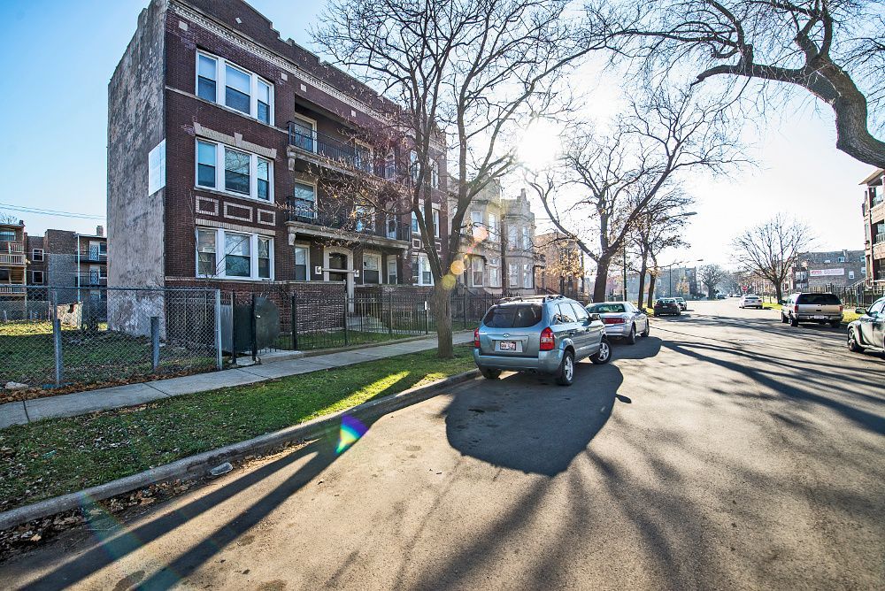 Apartment building on a sunny street with parked cars and bare trees.