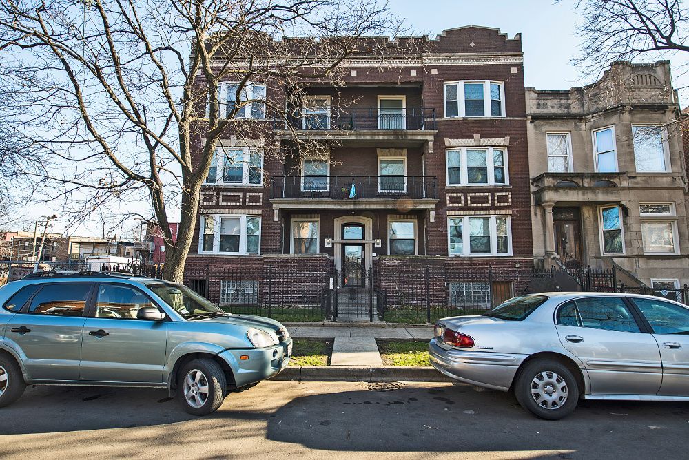 Apartment building with brick facade and balconies; parked cars on street.