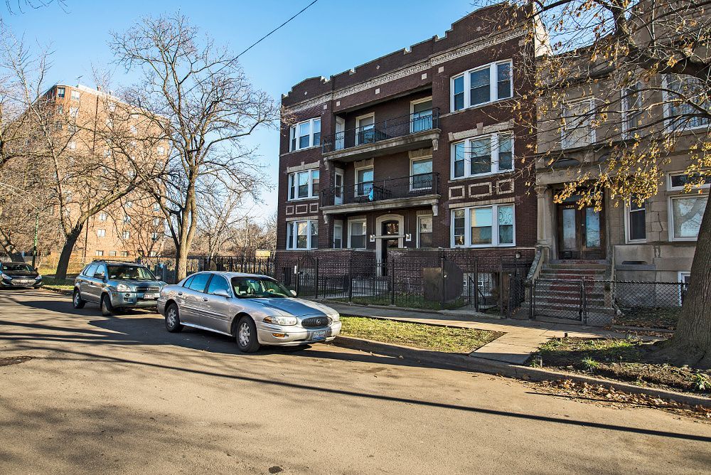 Apartment building on a tree-lined street with parked cars on a sunny day.