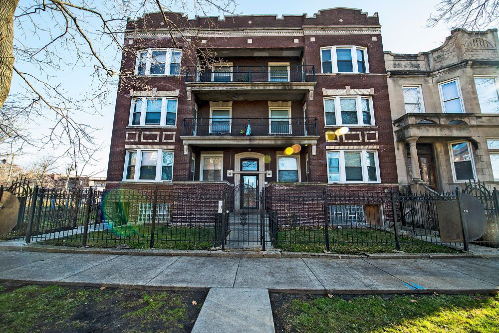 Apartment building, red brick, three stories, black iron fence in front, overcast sky.