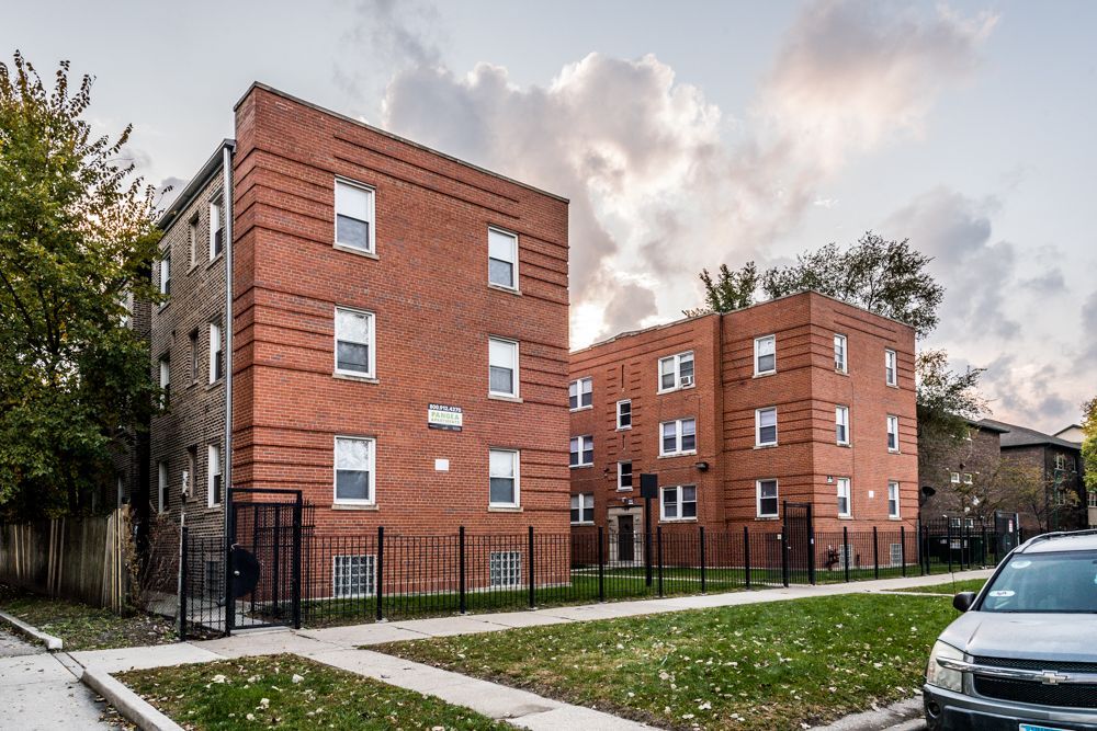 Brick apartment buildings with a cloudy sky and a car parked on the street.
