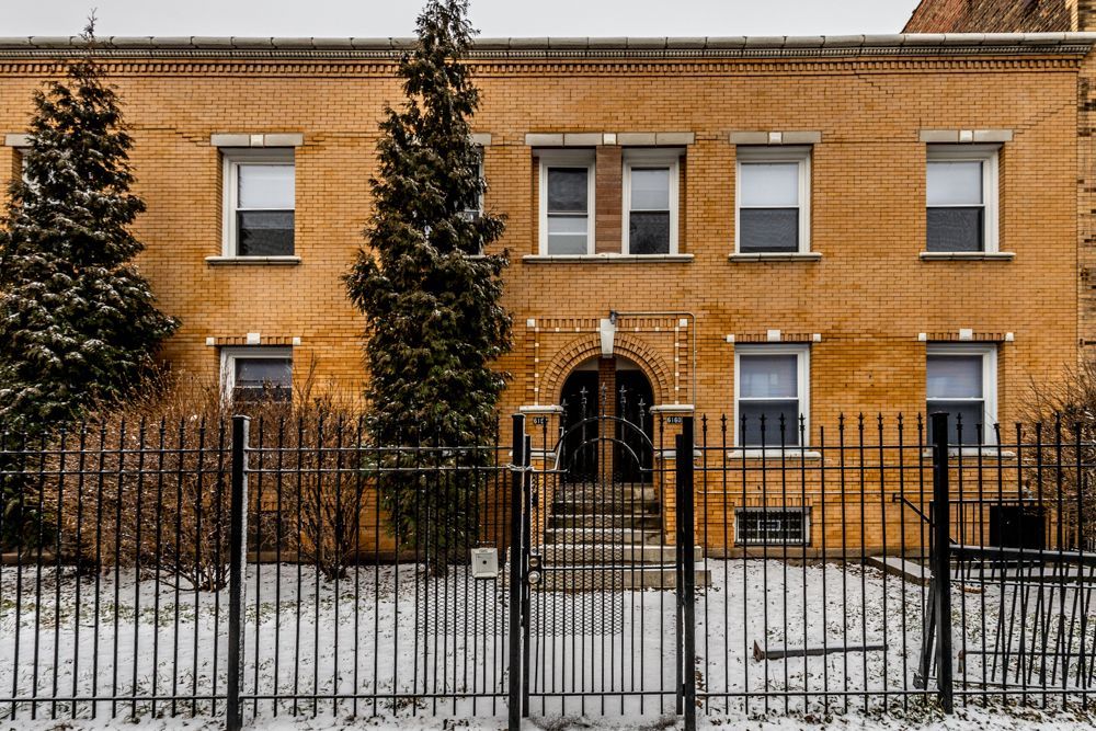 Brick apartment building with black wrought iron fence and gate, snow on the ground, trees.