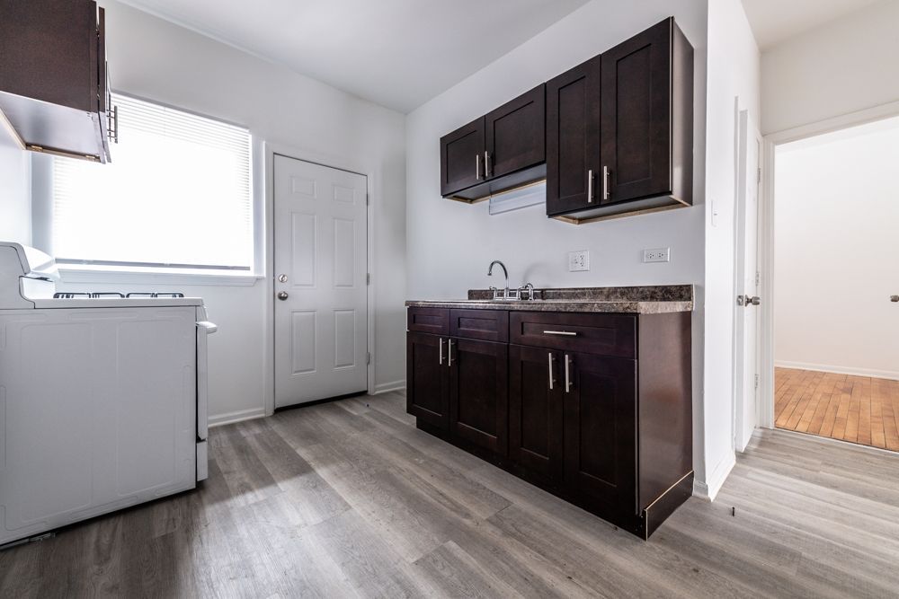 Small kitchen with dark cabinets, a white stove, and light wood-look flooring.