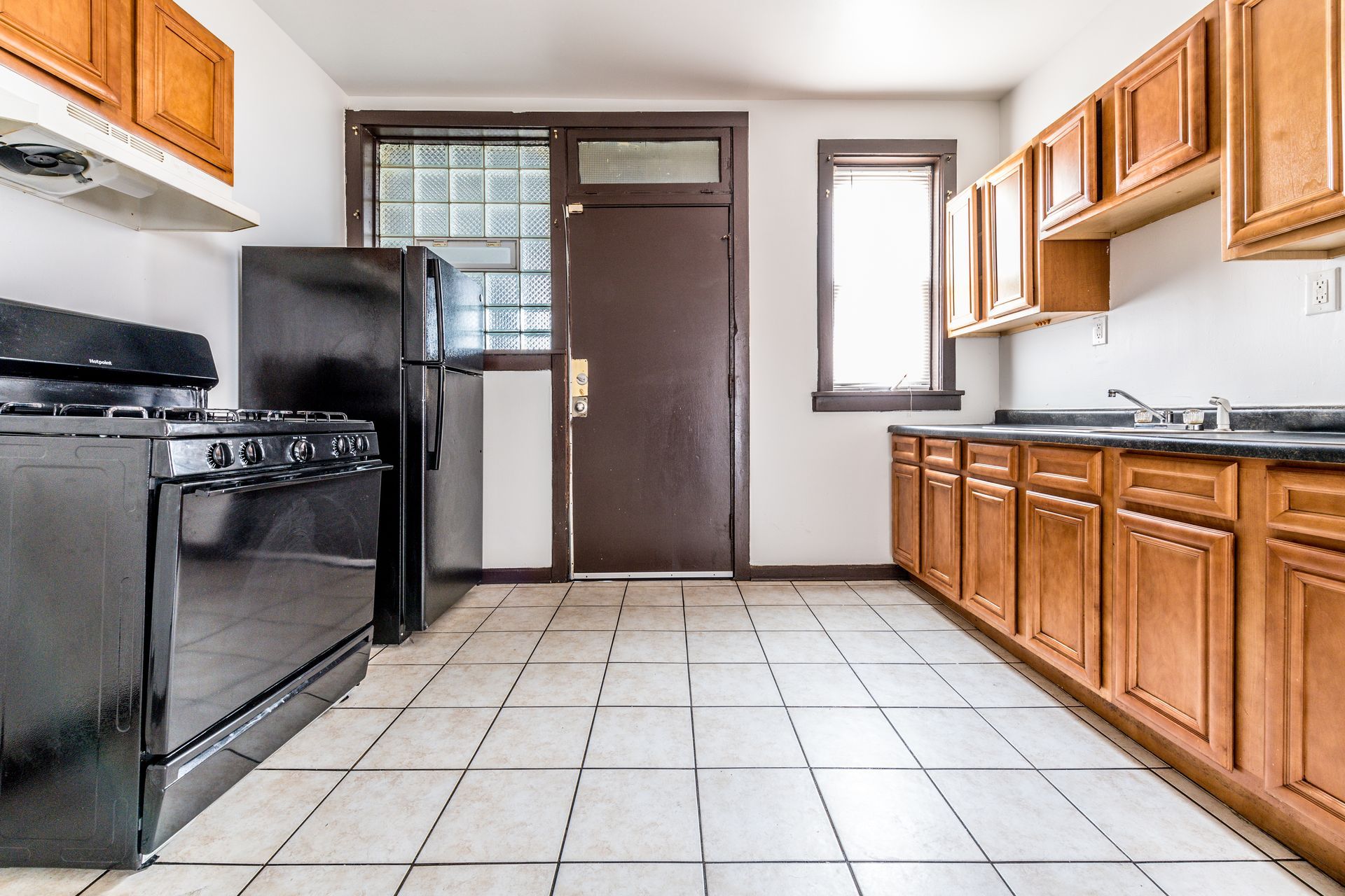 Kitchen with brown cabinets, black appliances, and white tile floor. A brown door and window are in the background.