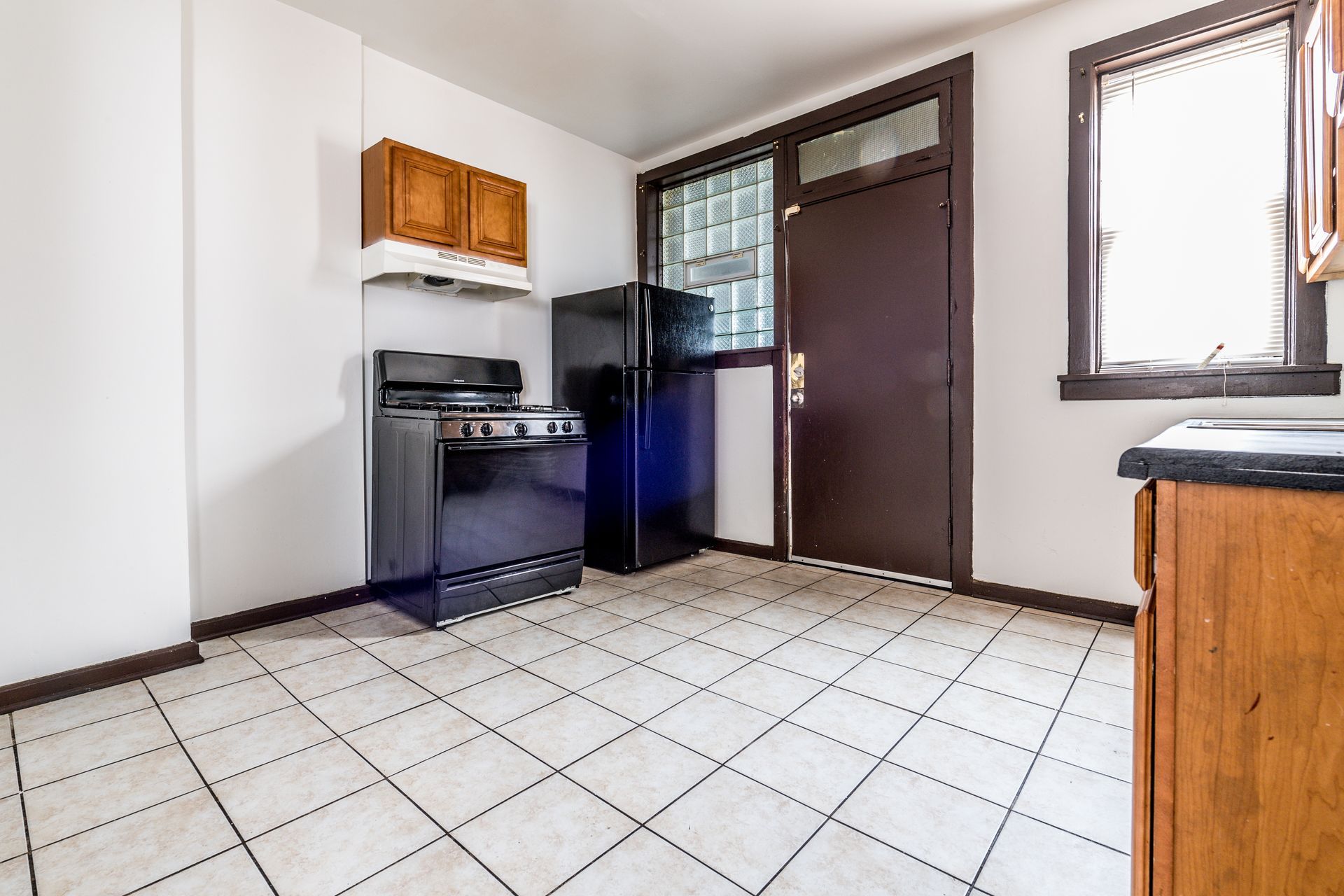 Kitchen with a black stove and refrigerator, light wood cabinets, and white tiled floor. Brown door and trim.