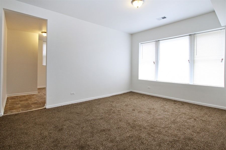 Empty room with brown carpet, white walls, and a large window with blinds.