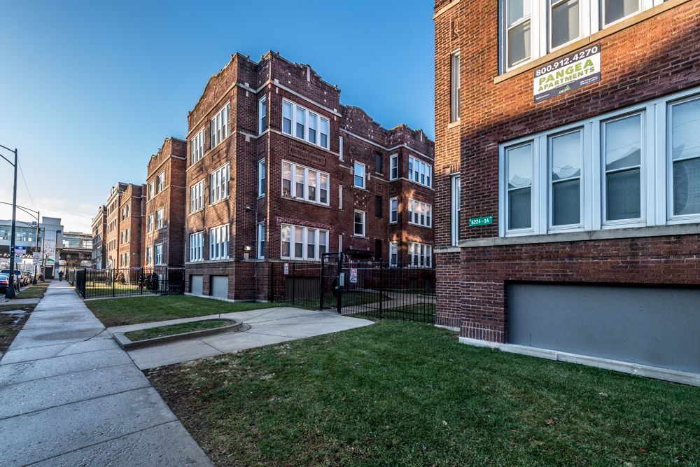 Brick apartment buildings with grassy yards and a sidewalk on a sunny day.