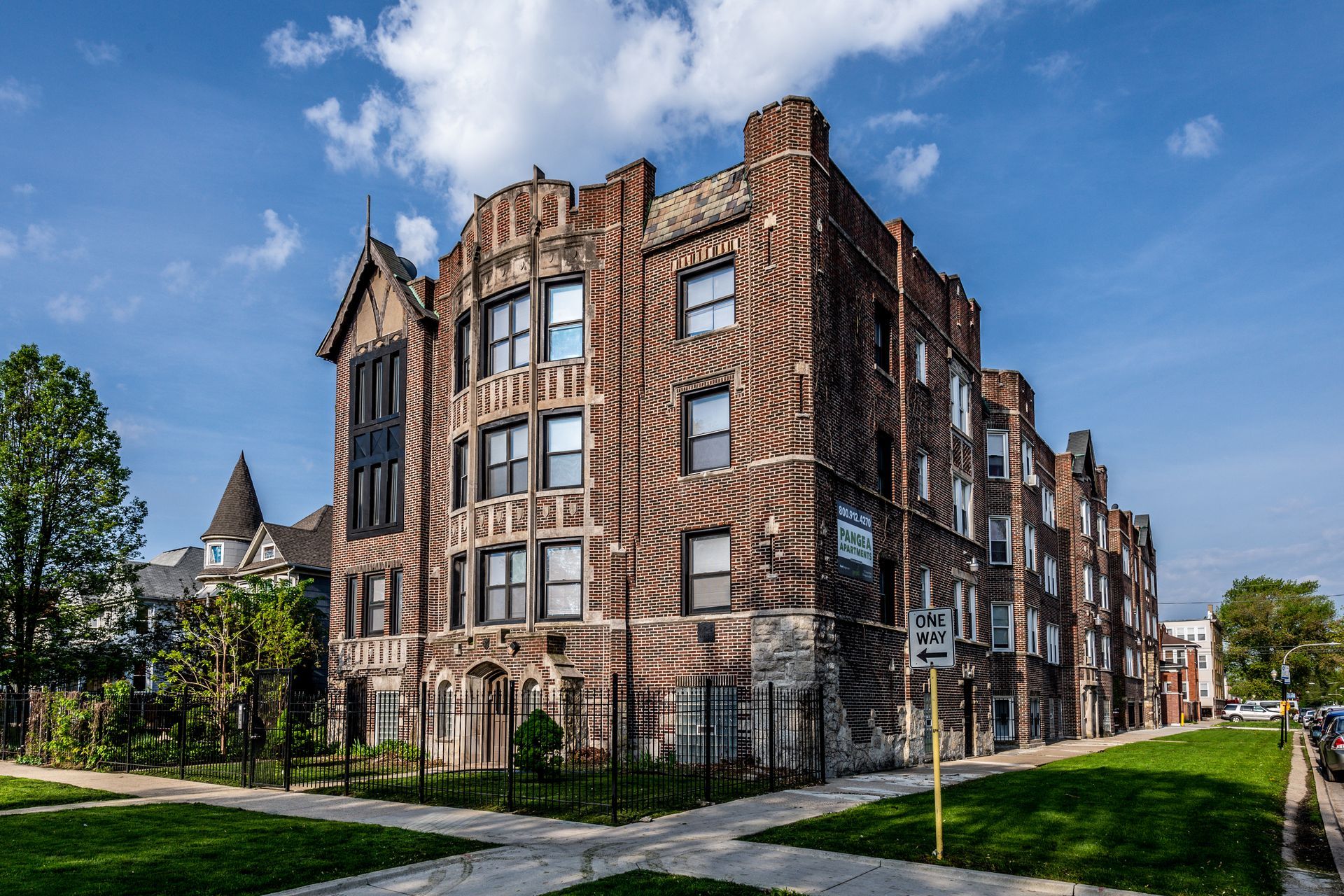 Brick apartment building on a corner lot, with dark trim, under a blue sky.