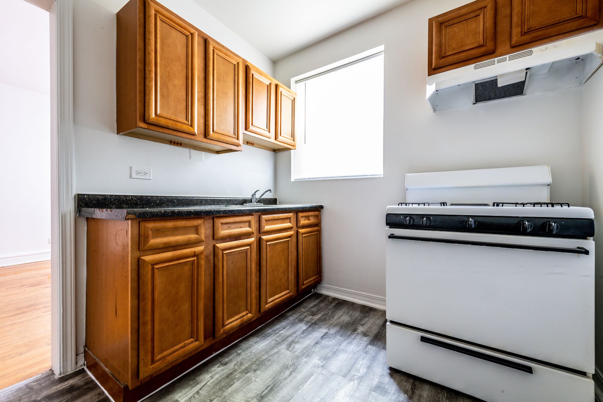 Kitchen with brown cabinets, white stove, and window; gray countertop and floor.