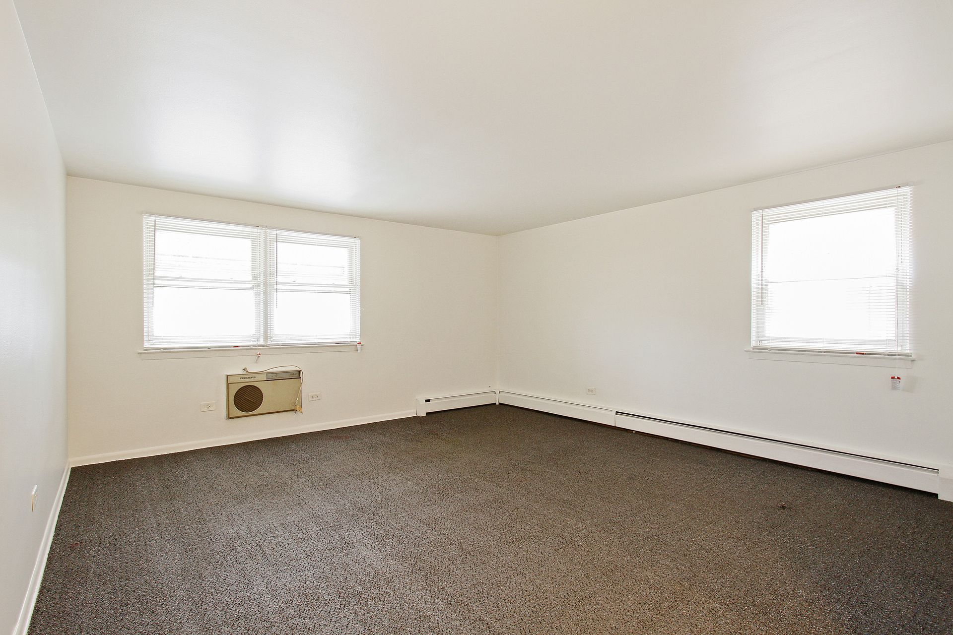 Empty room with brown carpet, two windows with blinds, and white walls.