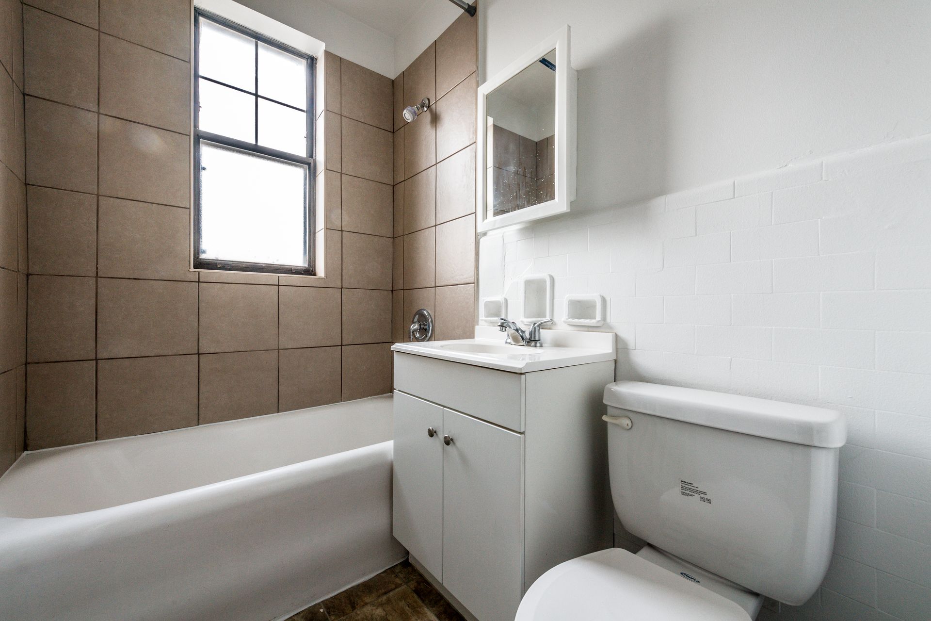 Bathroom with white tub, sink, toilet, and beige tile, and a window.