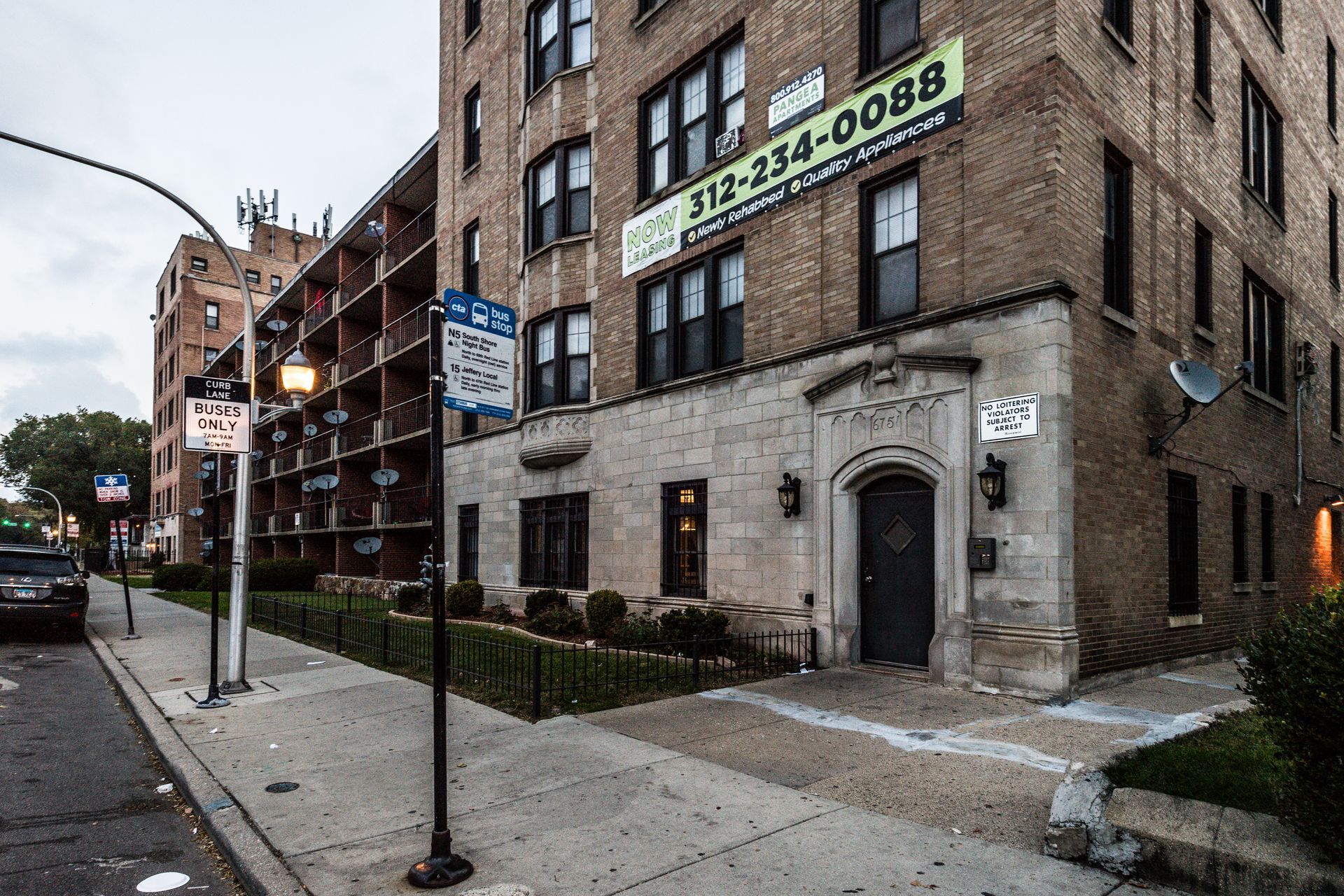 Apartment building exterior, brick and stone facade, sidewalk, street, overcast day.
