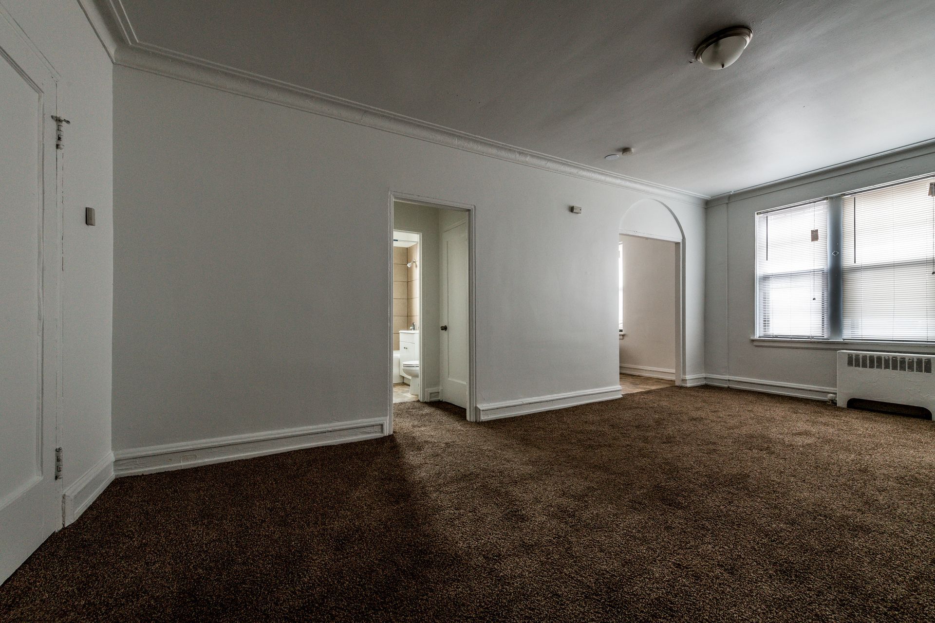 Empty room with brown carpet, white walls, two doorways, and a window.