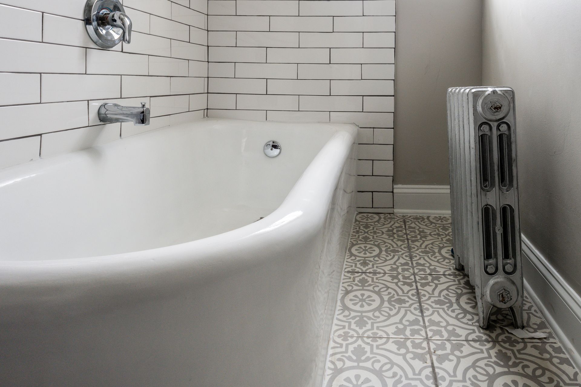 White bathtub with chrome fixtures, patterned floor, and radiator in bathroom.