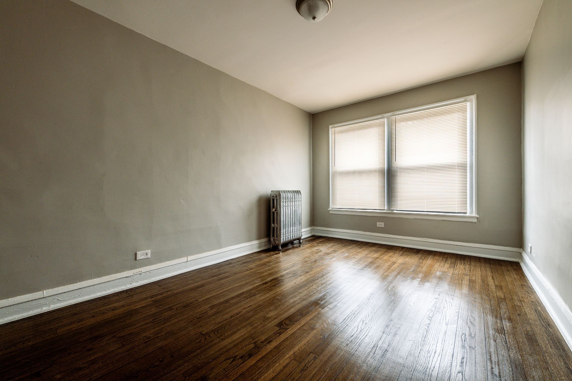 Empty room with hardwood floors, a window with blinds, and a radiator.