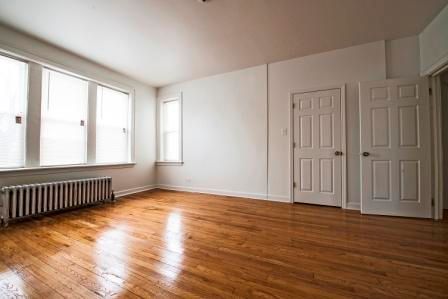 Empty room with hardwood floors, white walls, two doors, and a large window.