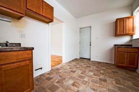 Empty kitchen with wood cabinets, brown countertop, and tiled floor. A door is visible.