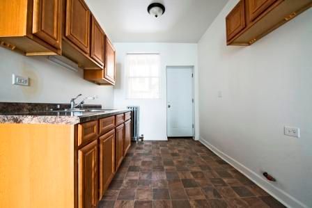 Kitchen with brown cabinets, countertops, and flooring, white walls, and a small window.
