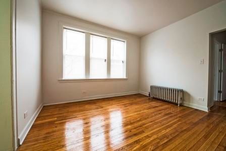 Empty room with hardwood floors, a radiator, and a window.