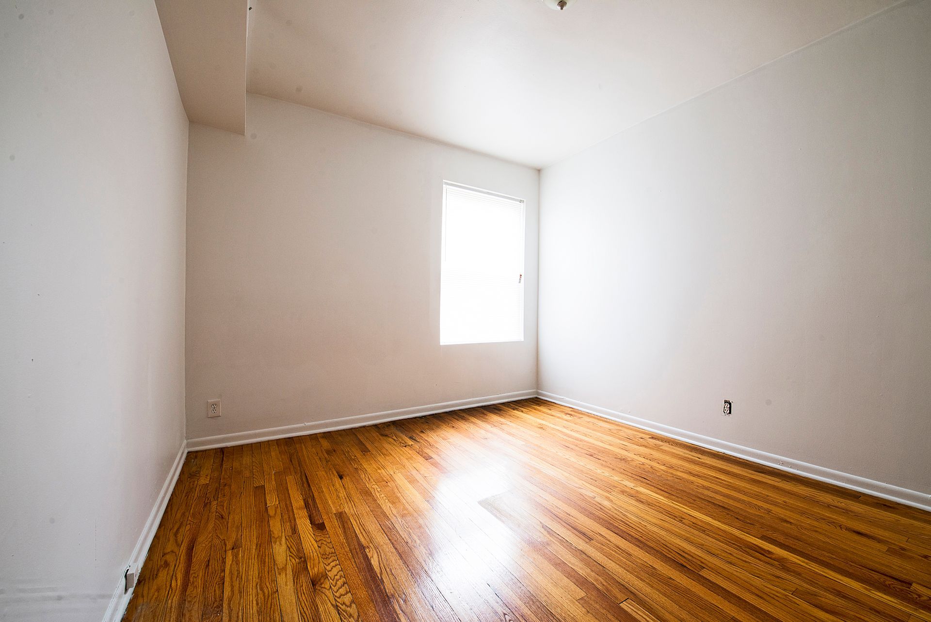 Empty room with hardwood floors, white walls, and a window.