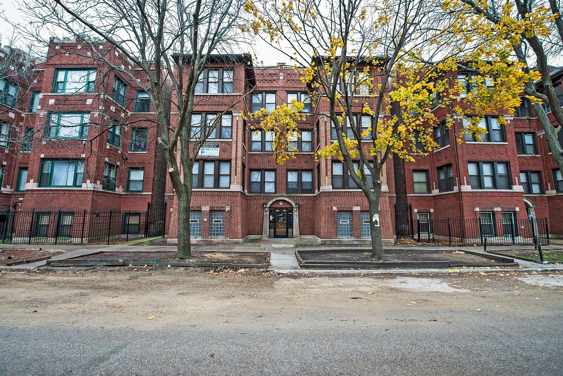 Red brick apartment building with trees in front, fall foliage.