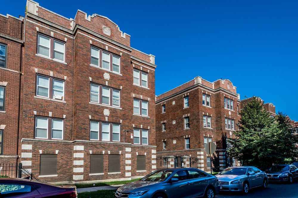 Brick apartment buildings with parked cars on a sunny street.