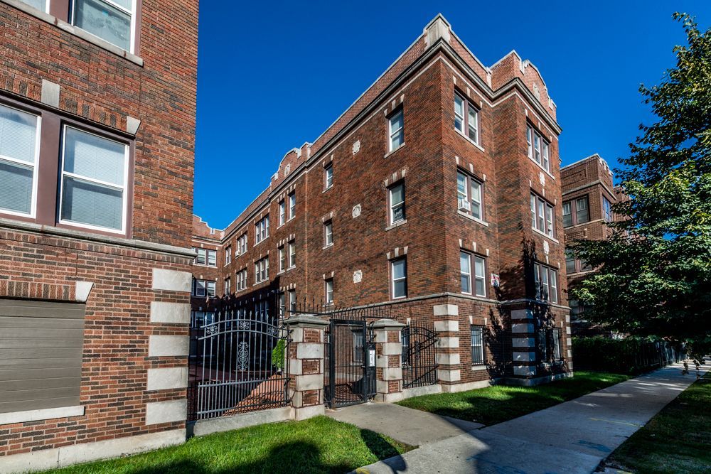 Brick apartment building on a sunny day with wrought iron fence and sidewalk.
