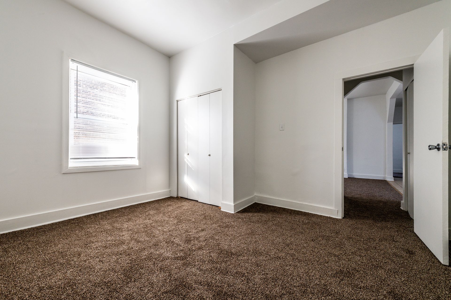 Empty room with brown carpet, white walls, closet, and a doorway.