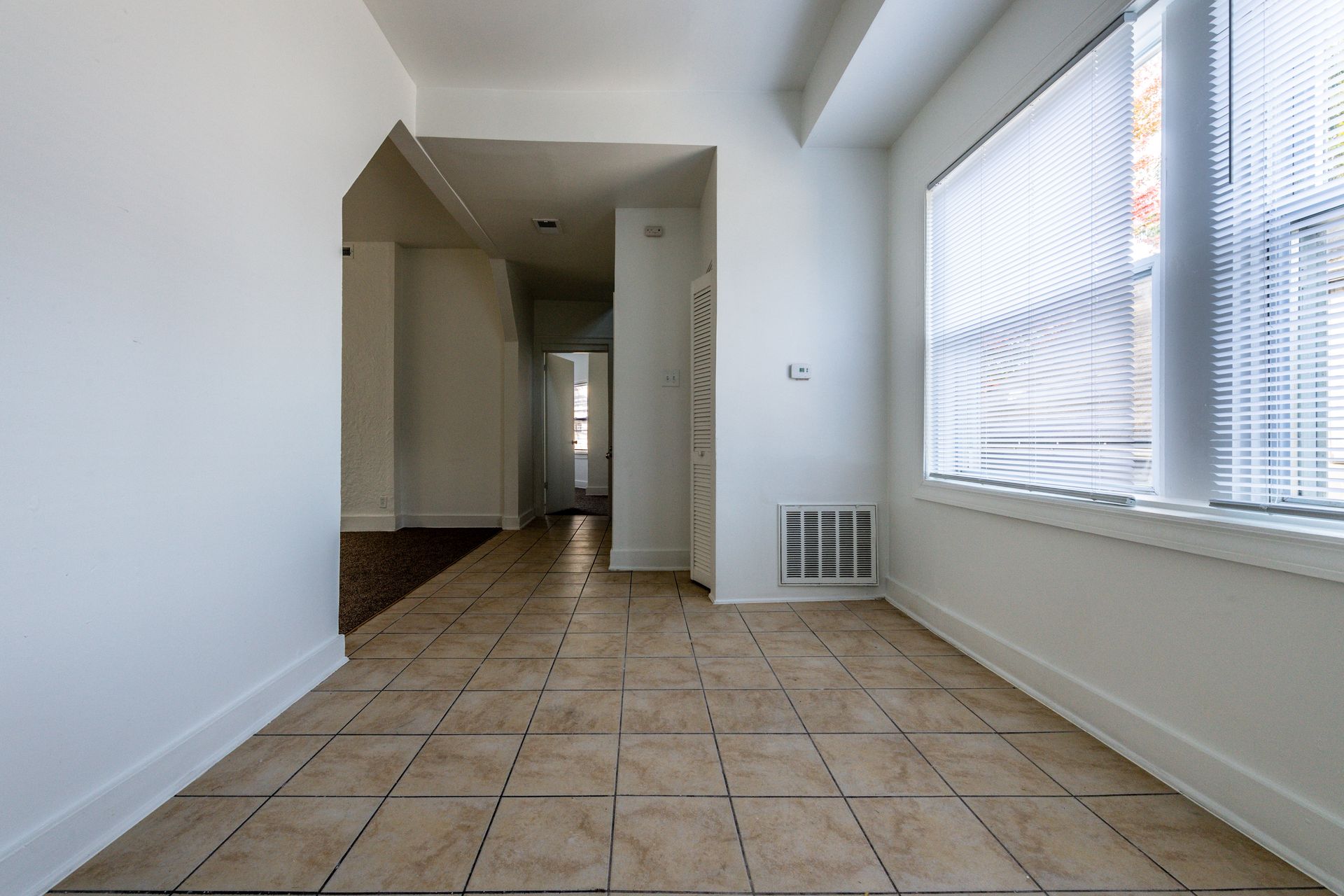 Hallway with tiled floor, white walls, and a large window with blinds.