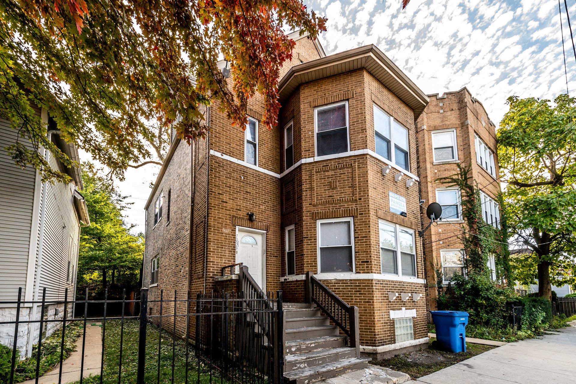 Brick multi-unit building with steps, fence, and trees.