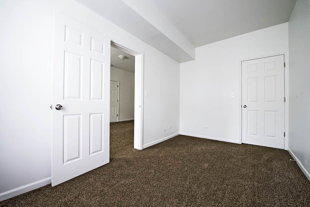 Empty room with brown carpet, white walls, and three white doors.